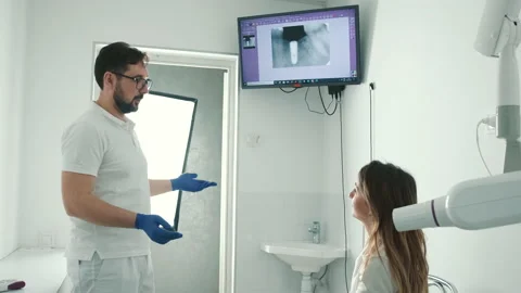 A gloved dentist makes an X-ray of the teeth and shows it to the patient on a Stock Footage 150934038