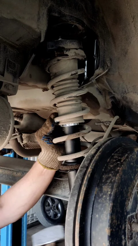 Gloved hand adjusting a new black shock absorber in car Stock Footage 333701276