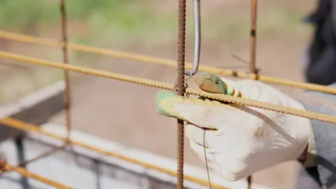 Gloved hand adjusting rusty steel rebar at outdoor construction site with wire Stock Footage 347692091