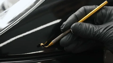 Gloved hand applying touch-up paint with a gold fluid writer pen on a black car Stock Footage 239277268