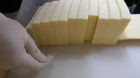 Gloved Hand Arranging Freshly Sliced Yellow Cheese Blocks on White Surface Video stock 343587526