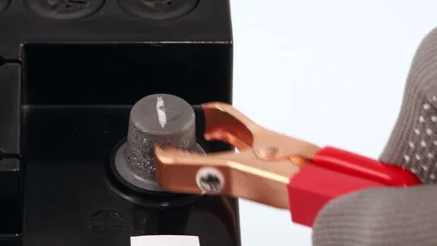 Gloved hand attaching a red alligator clamp to the positive terminal Stock Footage 321414972
