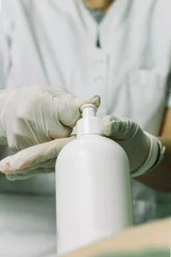Gloved hand with bottle of moisturizer preparing for massage. Stock Photos