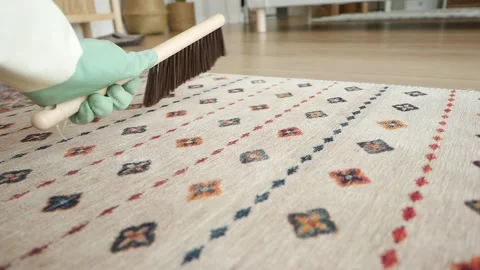 Gloved hand brushes patterned rug, cleaning home interior detail, slow motion Vídeos de archivo 332579623