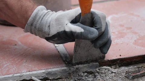 Gloved hand chiseling old ceramic tile during floor repair work Stock Footage 345600119