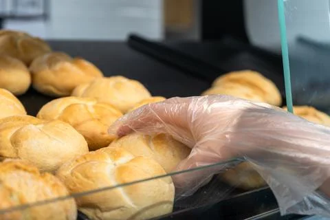 Gloved hand choosing fresh bread from bakery counter behind glass display Foto stock