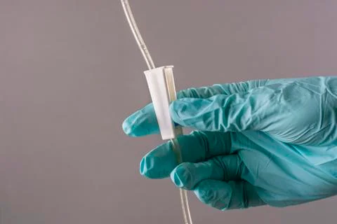 A gloved hand controls the rate of fluid intake of a medical dropper. Stock Photos
