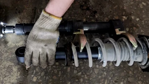 Gloved hand holding a car shock absorber with compressed spring Stock Footage 333701548