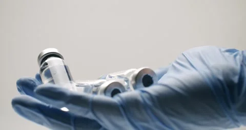 Gloved hand holding multiple transparent vaccine vials Stock Footage 343044491