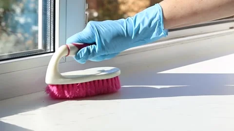 Gloved hand holding pink scrubbing brush over window sill with detergent sp.. Stock Footage 346784714