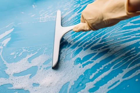 Gloved hand holding a squeegee upright on a foamy blue surface Stock Photos