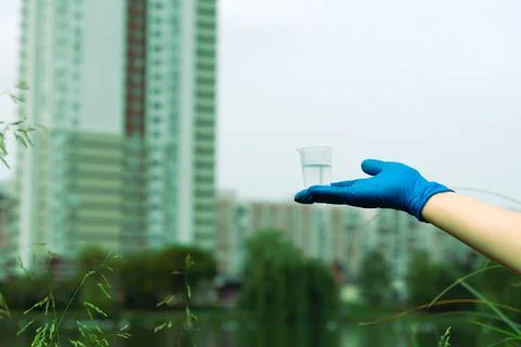 A gloved hand holds a beaker with a sample of water. Sampling from open water Stock Photos