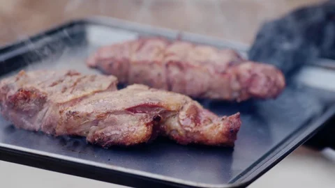 Gloved hand holds recently cooked cuts of meat on a tray outside Stock Footage 101612513