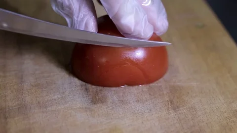 Gloved hand with a knife cuts a tomato quickly close up Stock Footage 93220687
