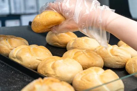 Gloved hand lifting fresh bread roll from tray in self service bakery section Fotos de archivo