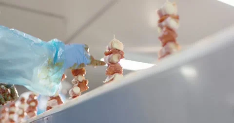 Gloved hand marinating bacon wrapped meat skewers in a food plant, Static Shot 動画素材 340031489