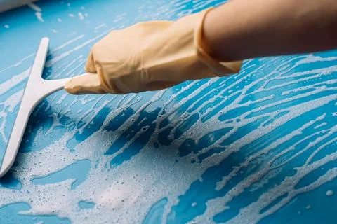 Gloved hand moving a squeegee along a foamy blue surface 스톡 사진