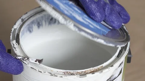 Gloved hand opening a can of white paint with can opener before starting paint Stock Footage 129139195
