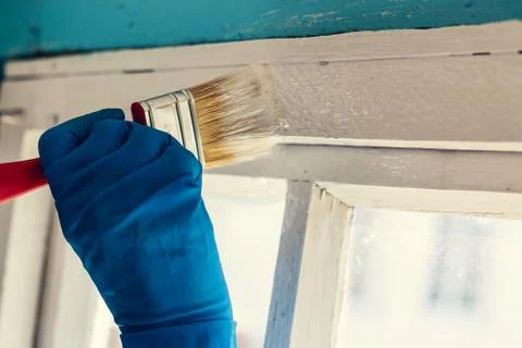 A gloved hand paints a window frame. Repair in the house. Services painter Foto stock