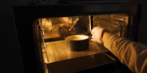 Gloved Hand Placing Round Cake Pan on Baking Sheet Inside Warm Lit Oven Stock-Footage 343588354