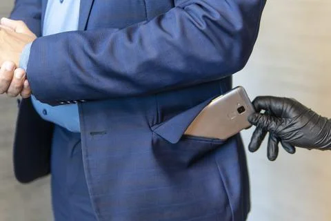 Gloved hand pulls out a mobile phone from a businessman's pocket. The concept Stock Photos