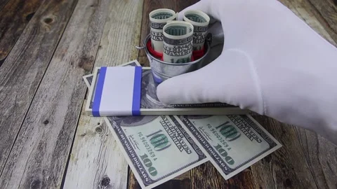 Gloved hand puts a bucket of 100 dollar banknotes on an envelope with banknotes Vídeo Stock 145535209