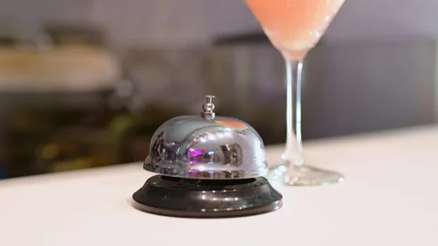 Gloved hand ringing a silver service bell on a bar counter with a pink cocktail Stock Footage 293530881