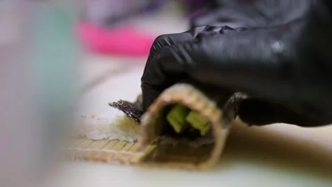 Gloved hand rolling sushi with rice, salmon, cucumber, and nori on a bamboo mat Stock Footage 293514469