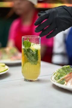Gloved hand serves mint lemon drink in glass Stock Photos