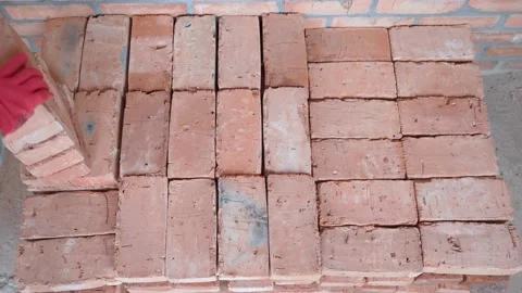A gloved hand stacks red ceramic bricks evenly.Working at a construction site Stock Footage 173347205