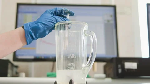 Gloved hand stirring white liquid inside clear measuring pitcher on lab Stock Footage 348262196