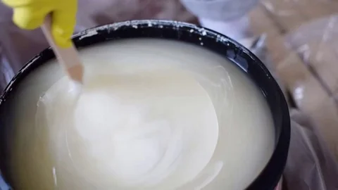 A gloved hand is stirring white paint in a bucket. Stock Footage 126321639