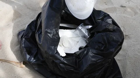 A gloved hand throws plastic into a black trash bag. Stock Footage 310941576