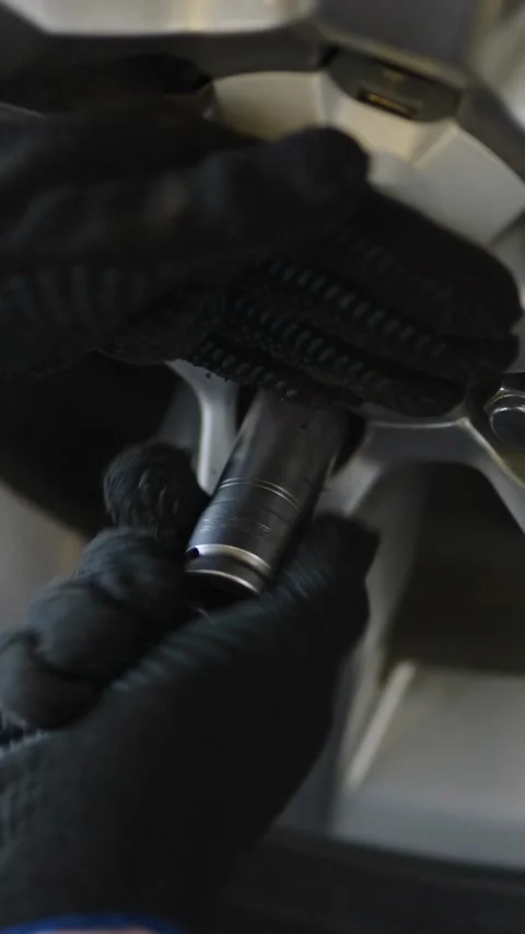 A gloved hand uses a socket wrench to tighten a lug nut on a silver car allo Stock Footage 336710635