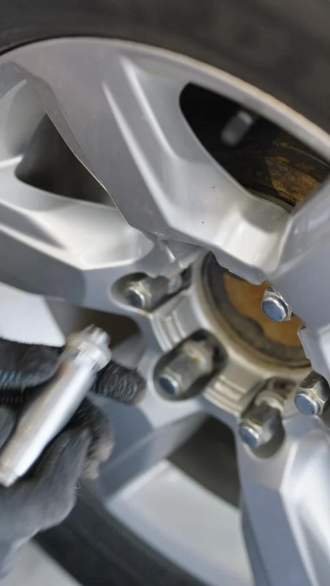 A gloved hand uses a socket wrench to tighten a lug nut on a silver car allo Stock Footage 336710666