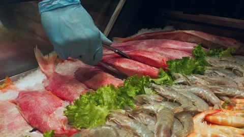 Gloved hand using tongs to pick up red snapper from ice display Stock Footage 336901005