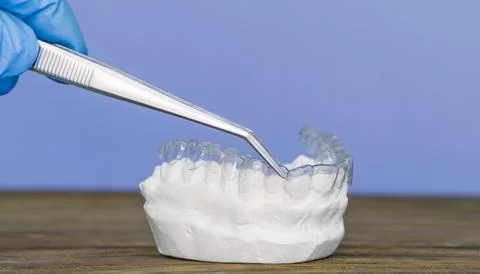 Gloved hand using tweezers to adjust a clear dental aligner on a plaster te.. Stock Photos