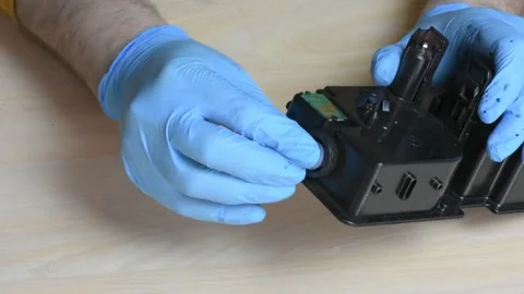 Gloved Hands Adjust Black Toner Cartridge on Wooden Table Stock Footage 319817244