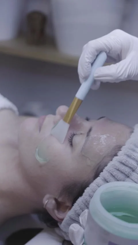 Gloved hands apply soothing mask with brush in gentle facial ritual Stock Footage 342821052