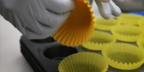 Gloved Hands Arranging Reusable Yellow Silicone Cupcake Liners in Muffin Baking Stock Footage 343588575