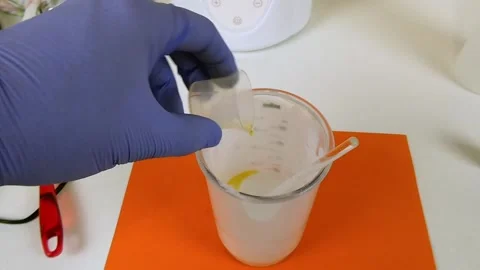 Gloved hands carefully mixing white powder and yellow liquid in a glass beaker Stock Footage 337738110