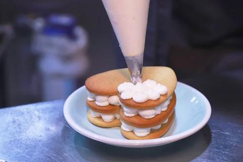 The gloved hands of the chef prepare a cream cake on a shiny table on a plate in Stock Photos