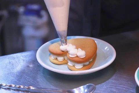 The gloved hands of the chef prepare a cream cake on a shiny table on a plate in Stock Photos