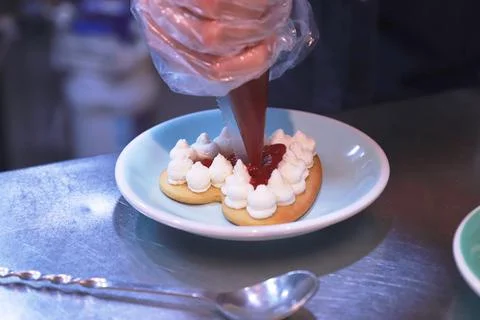 The gloved hands of the chef prepare a cream cake on a shiny table on a plate in Stock Photos