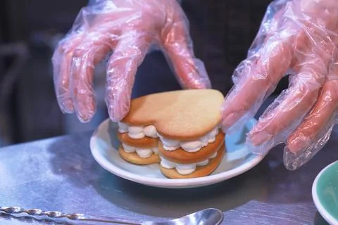 The gloved hands of the chef prepare a cream cake on a shiny table on a plate in Stock Photos