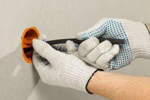 Gloved hands conduct the electrical cable into the socket box Stock Photos