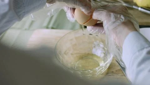 Gloved Hands Cracking a Fresh Egg over a Mixing Bowl 스톡 사진