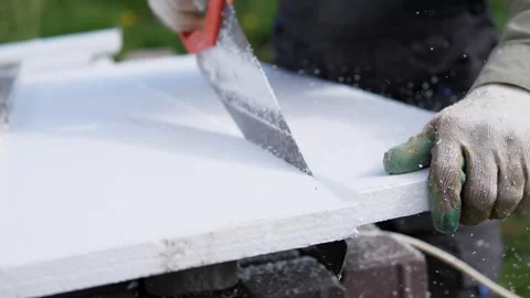 Gloved hands cut thick white foam insulation board with hand saw outdoors Stock Footage 344822035