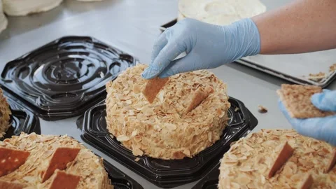 Gloved Hands Decorating Almond Layered Cake: Professional Bakery Preparation Stock Footage 321940037
