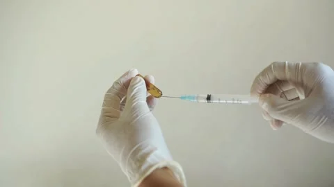 Gloved hands drawing liquid medication from an open glass ampoule Stock Footage 322205901